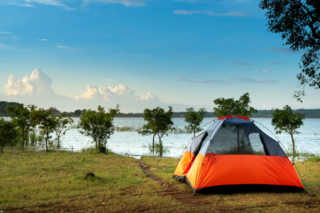 Peaceful lakeside scene with an orange camping tent and clear blue sky. Perfect outdoor adventure.